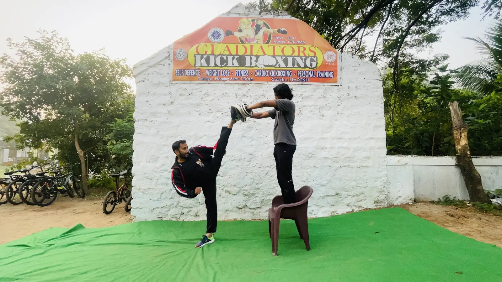 High kick on the green mat under the red and yellow Gladiators Kick Boxing board