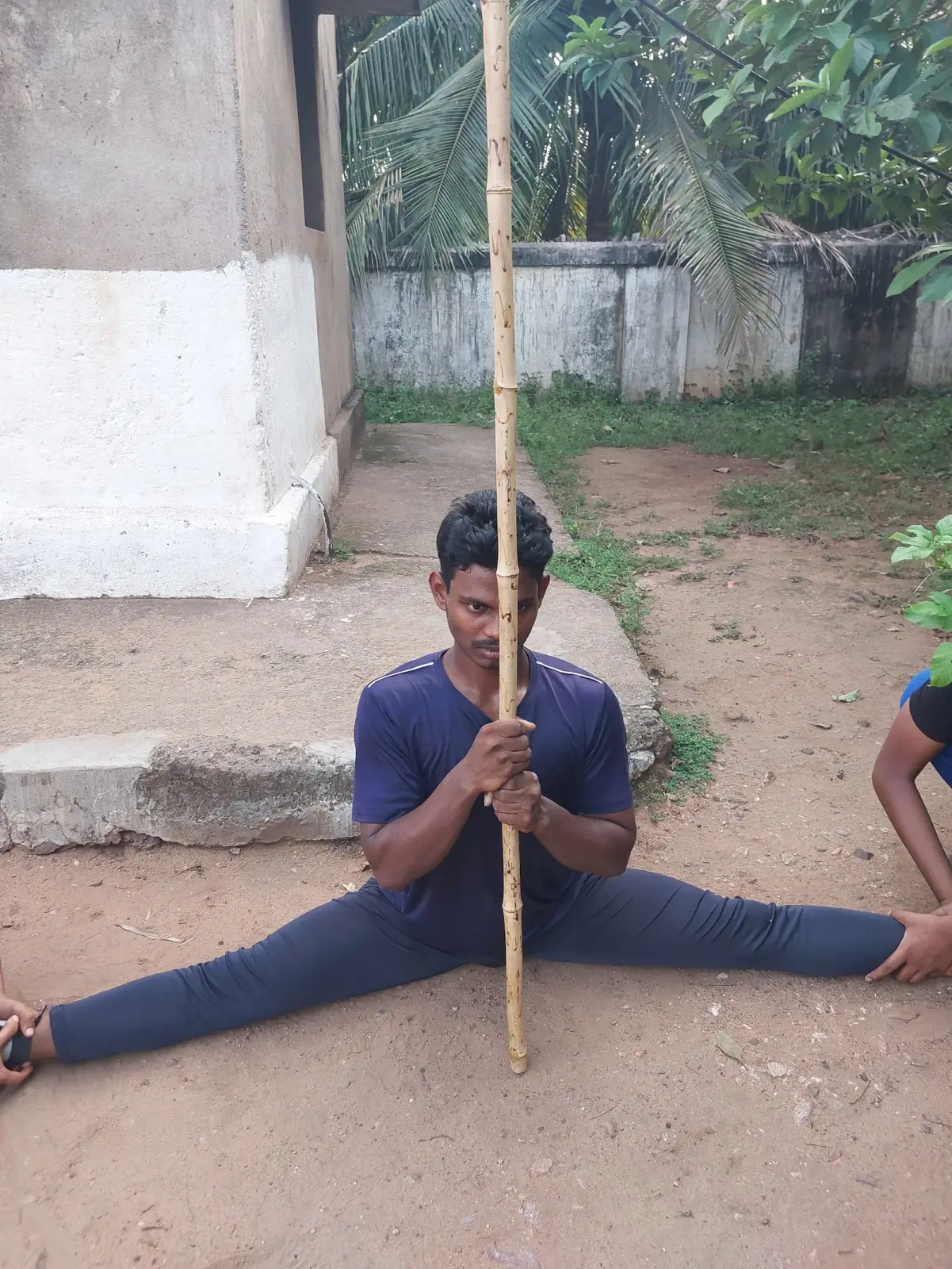 A student holding a full split on the ground with a training stick
