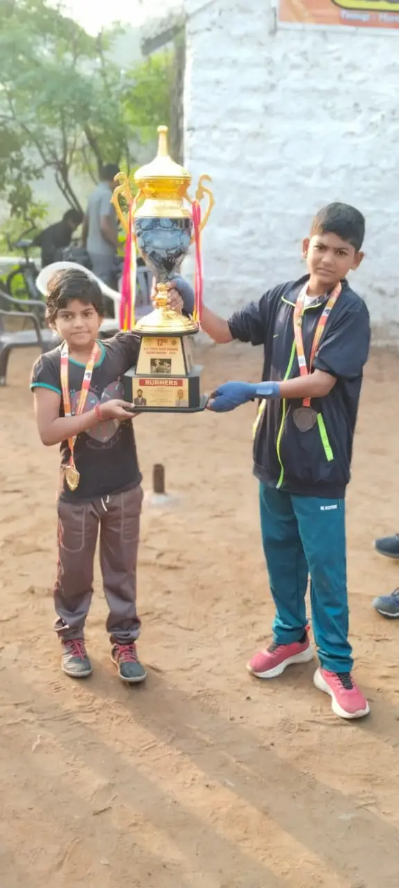 Two young students holding up a large trophy in the yard